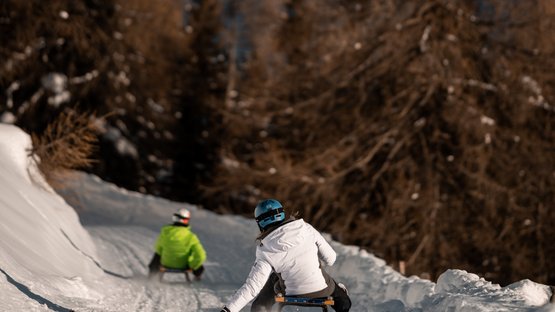 Die längste Rodelbahn Südtirols Personen rodeln auf verschneiter Bergstrecke mit Bergen im Hintergrund