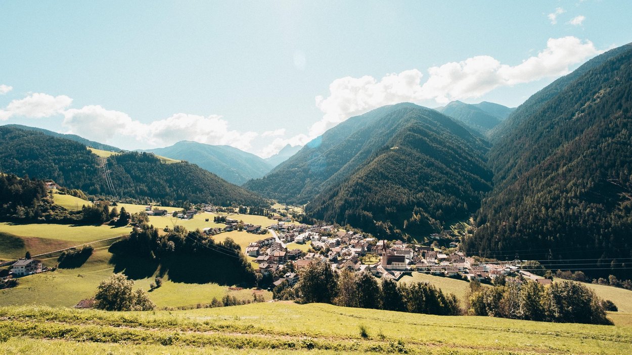 Hotels in Lüsen entdecken Blick auf ein Dorf im Tal umgeben von Bergen und grünen Wiesen bei Sonnenschein