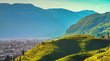 Hotel in Bozen gesucht? Finden Sie Ihre Traumunterkunft! Sonnige grüne Weinberge und Häuser vor Bergen und Stadt im Hintergrund
