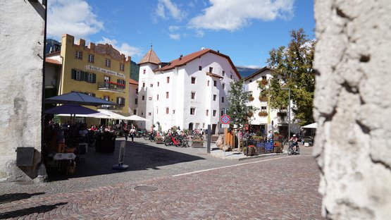 Hotel a Glorenza in Alto Adige Piazza affollata con edifici storici e caffè sotto un cielo azzurro