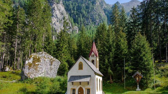 Hotels im Martelltal: schöne Tage verbringen Kleine Kapelle vor Nadelwald und Bergkulisse bei klarem Himmel