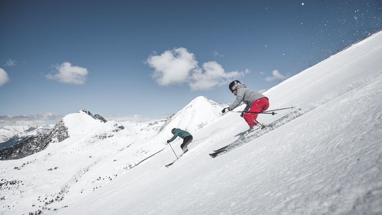 Meran 2000 – das perfekte Skigebiet für Familien Zwei Skifahrer auf schneebedecktem Berg bei sonnigem Himmel