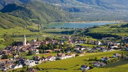 Hotel sulle Dolomiti Vista di un paese con chiesa, vigneti e un lago tra le montagne