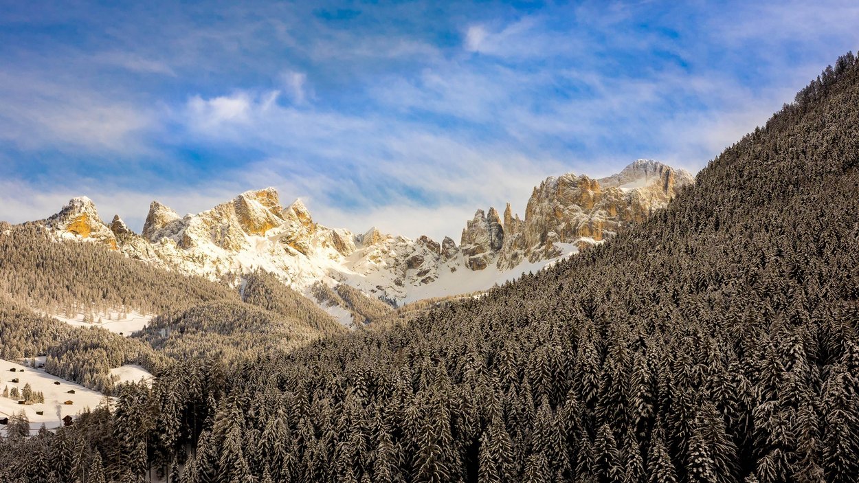 Hotel a Tires al Catinaccio Foresta di abeti innevata davanti a cime montuose imponenti e innevate sotto un cielo azzurro