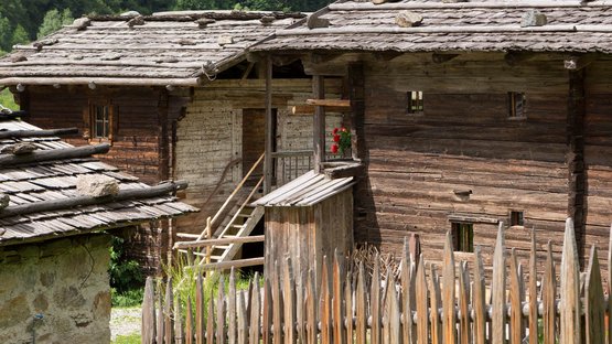 Das MuseumPasseier im Sandhof Altes Holzhaus mit Holzzaun und grüner Wiese in ländlicher Berglandschaft