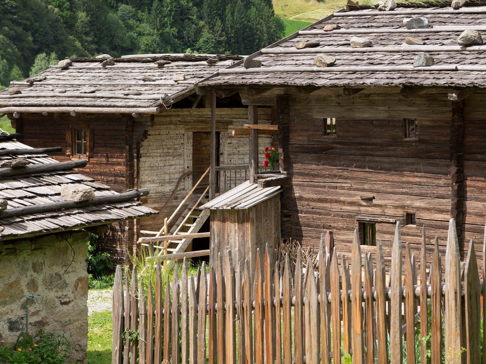 Das MuseumPasseier im Sandhof Altes Holzhaus mit Holzzaun und grüner Wiese in ländlicher Berglandschaft