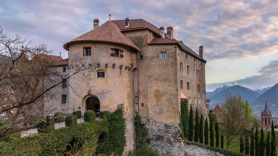 Hotel a Scena presso Merano Vecchio castello su una collina con vista sulla valle e montagne sotto un cielo nuvoloso