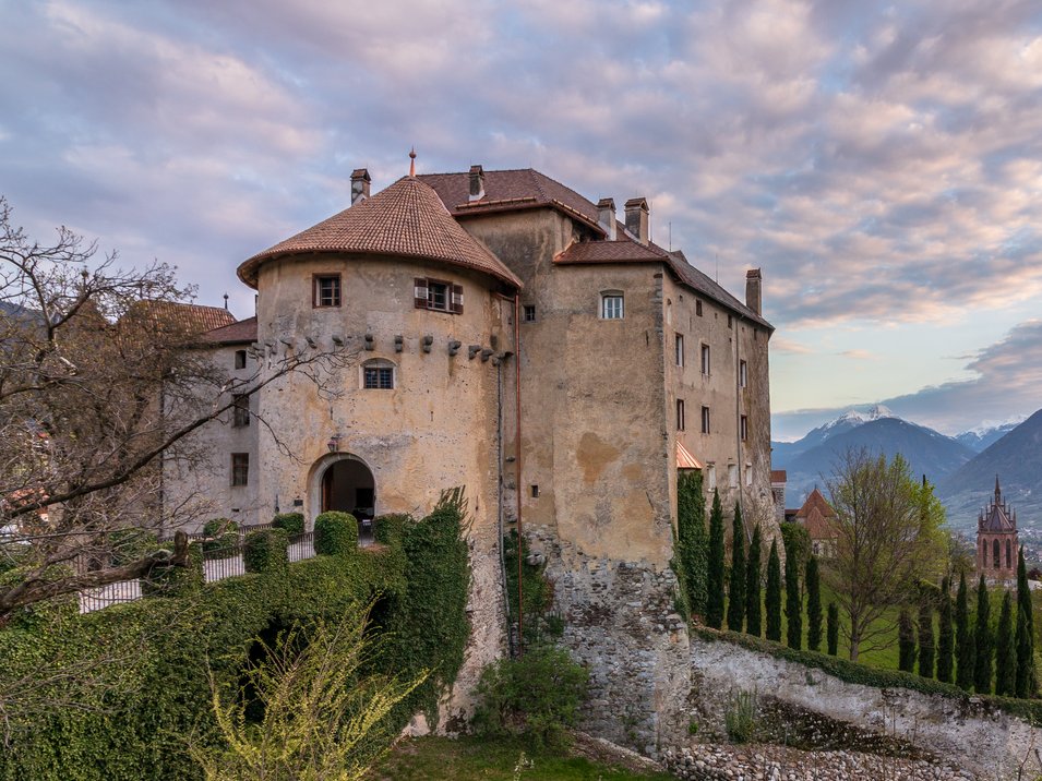 Hotel a Scena presso Merano Vecchio castello su una collina con vista sulla valle e montagne sotto un cielo nuvoloso