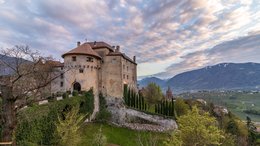Ihre Hotels in Meran in Südtirol: Hotels im Meraner Land Altes Schloss auf einem Hügel mit Blick auf Tal und Berge bei bewölktem Himmel