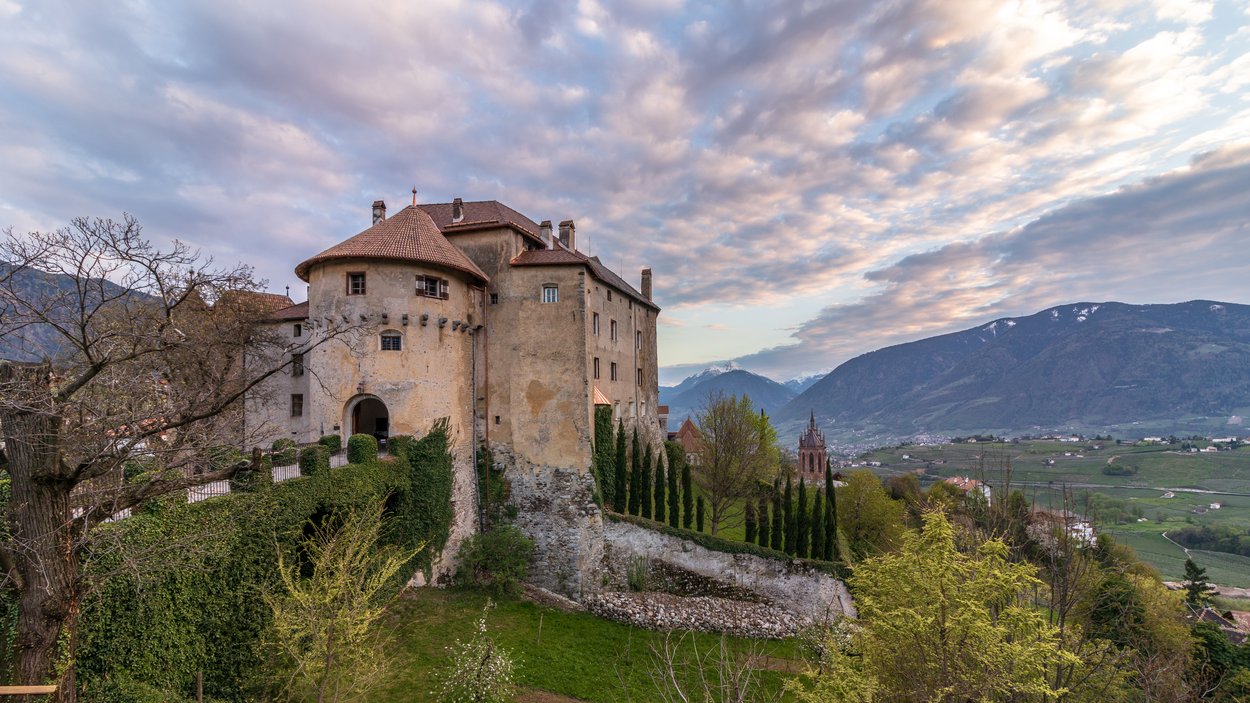 I castelli più belli dell’Alto Adige: Castello di Scena Vecchio castello su una collina con vista sulla valle e montagne sotto un cielo nuvoloso