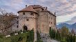 Hotel a Scena presso Merano Vecchio castello su una collina con vista sulla valle e montagne sotto un cielo nuvoloso