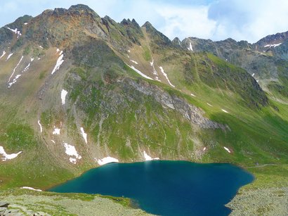 Lago artificiale di Fortezza Lago alpino con neve sulle pendici verdi sotto cielo nuvoloso