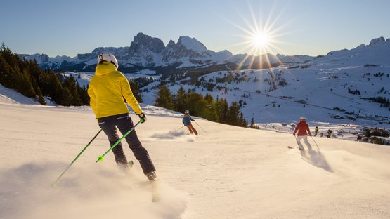 Skihotels in Südtirol - Pistenglück und Winterspaß Vier Skifahrer fahren bei sonnigem Wetter auf verschneiter Bergpiste
