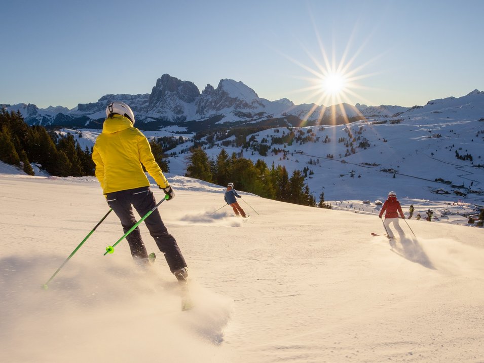 Hotel sulle piste da sci in Trentino-Alto Adige Quattro sciatori scendono una pista innevata con il sole splendente