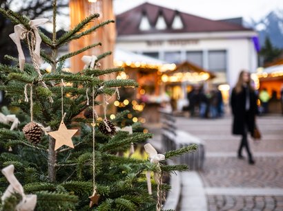 Il mercatino di Natale di Bolzano Albero di Natale con stelle di legno e pigne davanti a mercato natalizio illuminato