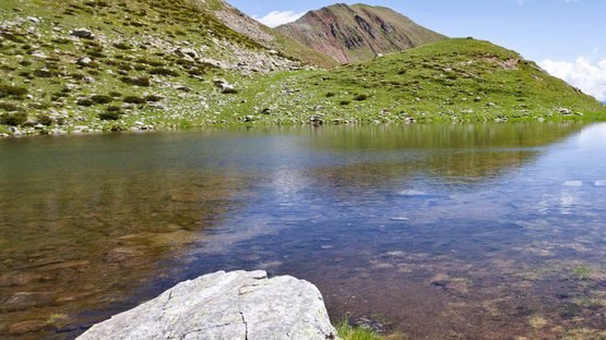 Tra la Val Venosta e la Val d’Ultimo Escursionista accanto a un lago di montagna con erba verde e cielo azzurro