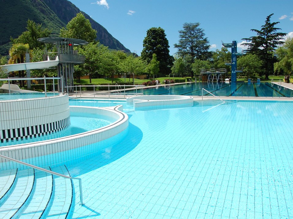 Lido di Bolzano: punto di ritrovo per grandi e piccini Piscina all'aperto vuota con scivoli, trampolini e montagne sullo sfondo