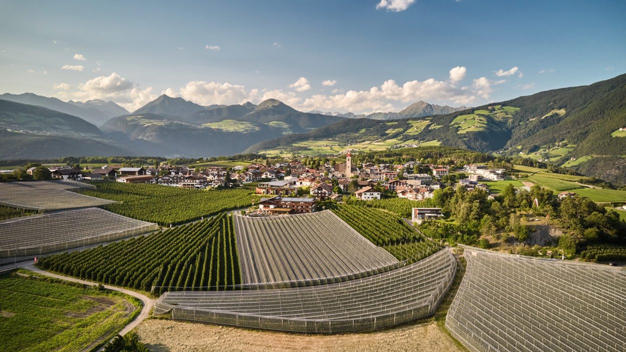 Hotel a Naz-Sciaves Vista di un villaggio e campi agricoli verdi davanti a una catena montuosa