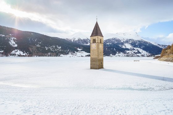 Reschensee: Naturparadies in Südtirol Kirchturm ragt aus zugefrorenem See mit schneebedeckten Bergen im Hintergrund