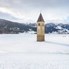 Skitour: Oberbachernspitze Kirchturm ragt aus zugefrorenem See mit schneebedeckten Bergen im Hintergrund