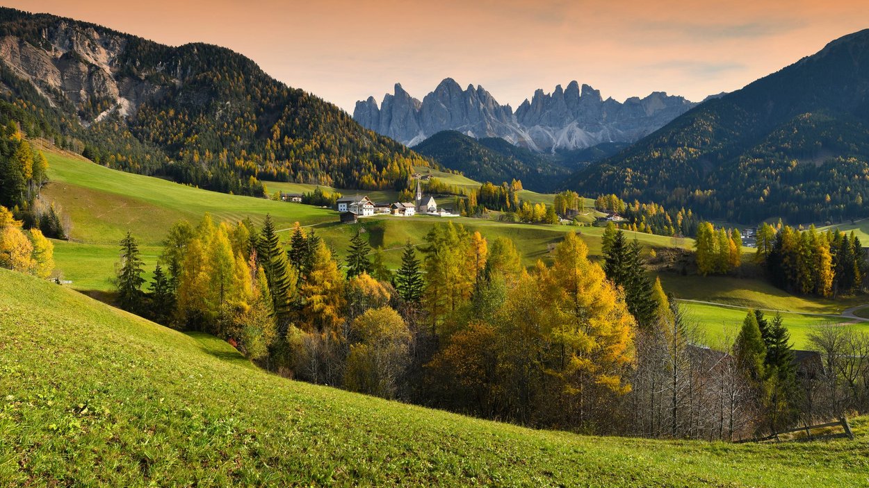 Hotels Villnöss: Dolomiten erleben Herbstliche Berglandschaft mit Dorf, grünen Wiesen und bewaldeten Hügeln