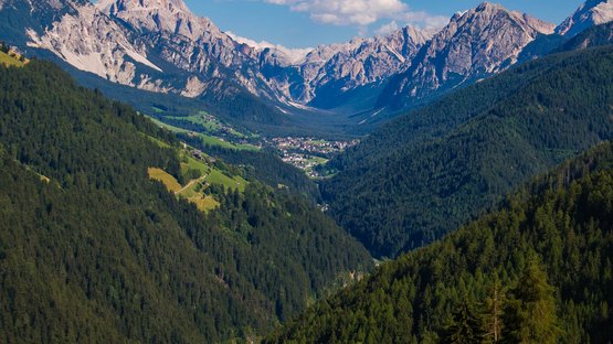 Charmante Hotels in St. Vigil in den Dolomiten Blick auf ein Dorf in einem bewaldeten Tal mit hohen Bergen im Hintergrund