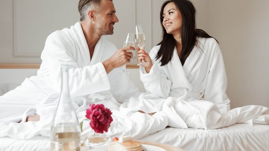 Hotel romantici in Alto Adige Coppia in accappatoi brinda a letto con calici di spumante