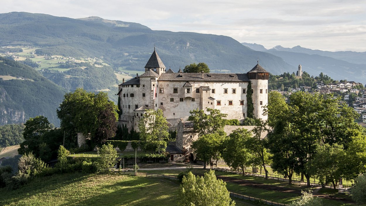 Castel Prösels a Fiè allo Sciliar Castello storico su una collina con alberi verdi e montagne sullo sfondo