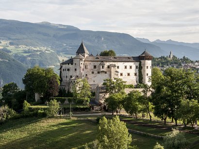 Hotel a Castelrotto sull’Alpe di Siusi Castello storico su una collina con alberi verdi e montagne sullo sfondo