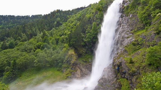 Hotel a Parcines a Merano e dintorni Alta cascata che scende accanto a una montagna boscosa in paesaggio nebbioso