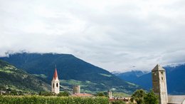 Hotel a Glorenza in Alto Adige Villaggio con campanili davanti a montagne boschive sotto cielo nuvoloso