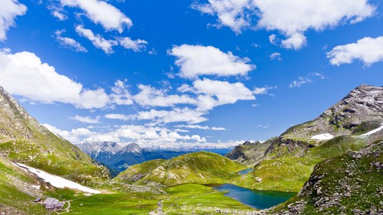Wandern und schlemmen auf der Oberkaser Alm Berglandschaft mit See, grünen Wiesen und blauem Himmel mit Wolken