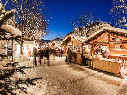 Hotels in St. Lorenzen: willkommen im Pustertal! Weihnachtsmarkt mit verschneiten Ständen und Besuchern bei Abenddämmerung