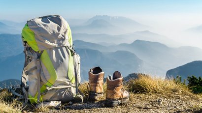 Hörspielwanderungen am Latemar Rucksack und Wanderschuhe auf einem Berg mit Nebel und Gipfeln im Hintergrund