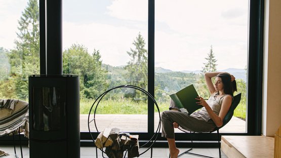 Appartamenti vacanze in Alto Adige Donna legge rilassata davanti a una grande finestra con vista su bosco e montagne