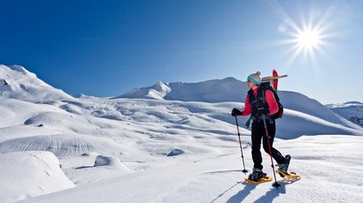 Der Labyrinthsteig Frau mit Schneeschuhen wandert auf schneebedecktem Berg bei sonnigem Himmel