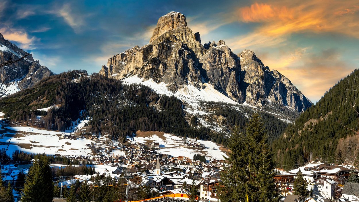 Ciaspolate in Val Gardena Villaggio con case innevate ai piedi di una grande montagna al tramonto