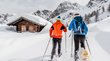 Schneeschuhwandern in Südtirol: Die Natur ruft! Zwei Personen beim Schneeschuhwandern vor einer schneebedeckten Hütte in den Bergen