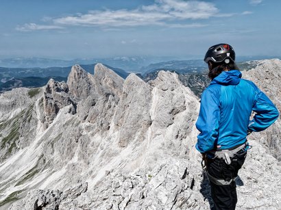Via ferrata sul Catinaccio d’Antermoia Alpinista con giacca blu e casco osserva le cime rocciose sulle Alpi