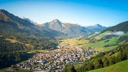 Hotel sulle Dolomiti Veduta di un villaggio in una valle verde circondata da montagne con cielo sereno