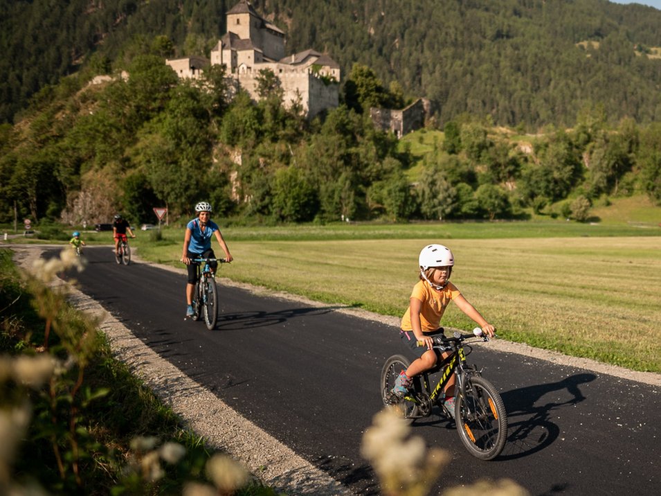 Schloss Reifenstein bei Sterzing Kind und Erwachsene fahren mit Helm auf Fahrrädern auf einem Weg mit Burg im Hintergrund