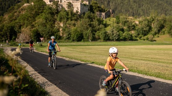 Schloss Reifenstein bei Sterzing Kind und Erwachsene fahren mit Helm auf Fahrrädern auf einem Weg mit Burg im Hintergrund