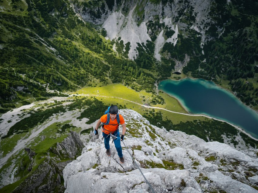 Hotel in Alto Adige 😎☀️ Per vacanze indimenticabili Alpinista con maglia arancione arrampicata su roccia con vista su lago e natura verde
