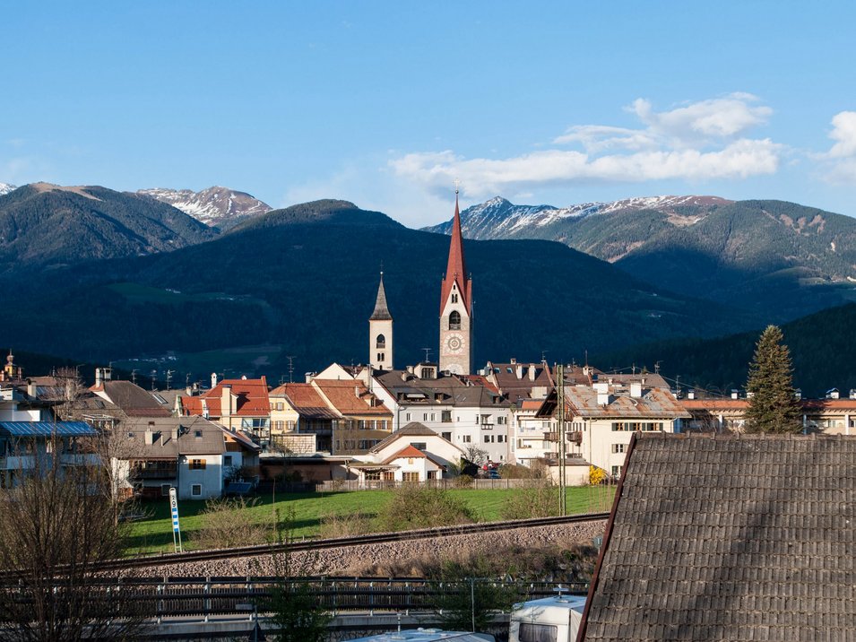 Hotels in St. Lorenzen: willkommen im Pustertal! Blick auf eine Stadt mit Kirchen und Bergen im Hintergrund bei klarem Himmel