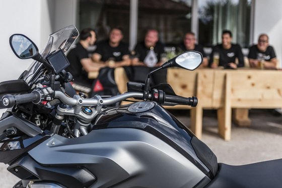 Ein Hotel furs Motorrad in Südtirol – der Hit! Motorrad im Vordergrund, Menschen sitzen im Hintergrund an einem Holztisch