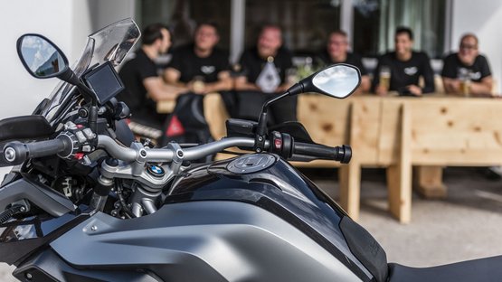 Den Jaufenpass auf dem Motorrad für sich entdecken Motorrad im Vordergrund, Menschen sitzen im Hintergrund an einem Holztisch