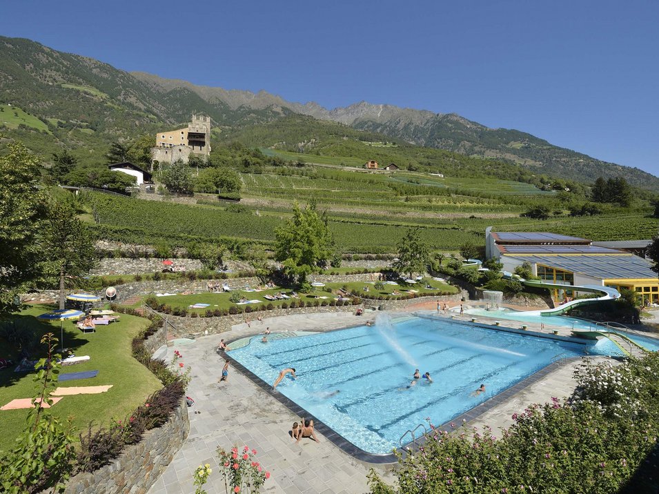 Das Erlebnisbad in Naturns Schwimmbad mit Wasserrutsche in bergiger Landschaft und Schloss im Hintergrund