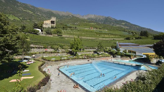 Das Erlebnisbad in Naturns Schwimmbad mit Wasserrutsche in bergiger Landschaft und Schloss im Hintergrund