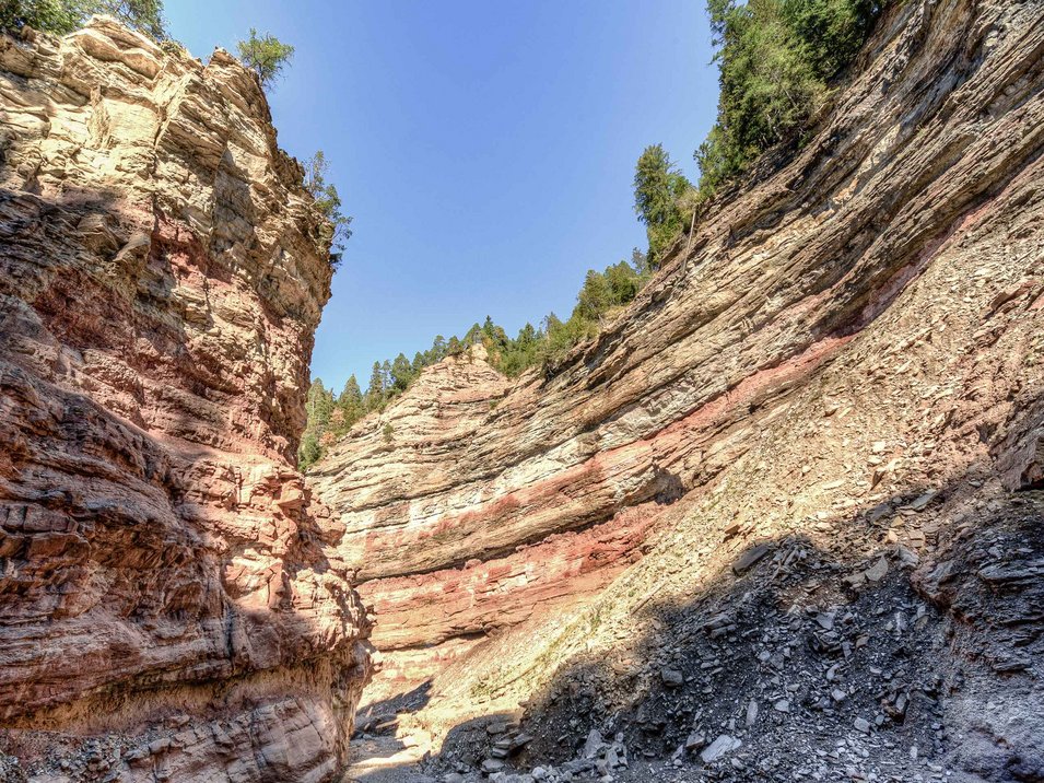 Centro visitatori GEOPARC Bletterbach Formazione rocciosa con strati di rocce diverse in una gola sotto cielo blu