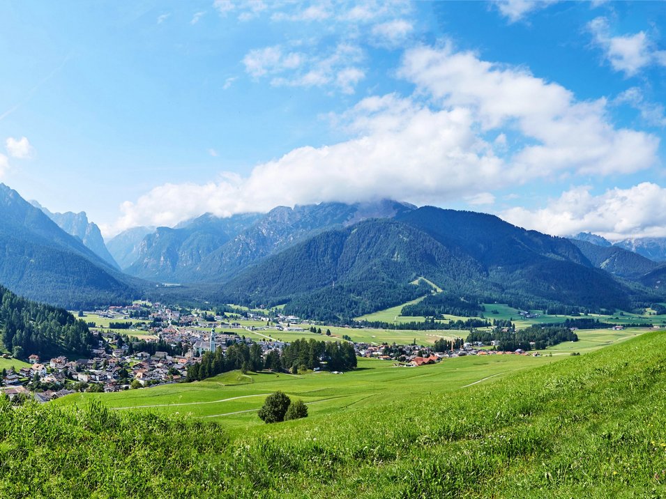 Der Falzaregopass Grünes Tal mit Dorf vor bewaldeten Bergen unter blauem Himmel